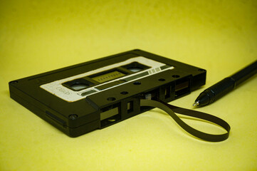 closeup of vintage audio cassette with magnetic band outside rewound with pen on yellow background