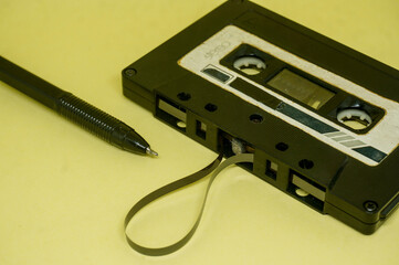 closeup of vintage audio cassette with magnetic band outside rewound with pen on yellow background