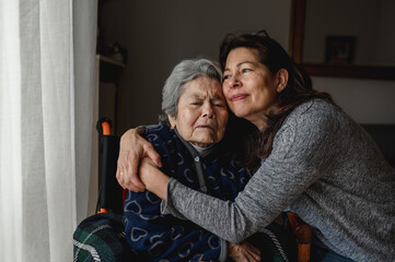 Portrait of woman in wheelchair hugging daughter with positive face. Third age, Home care concept.