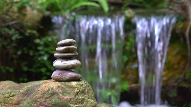 Pyramid of pebble stones next to waterfall. Zen or wellness concept.