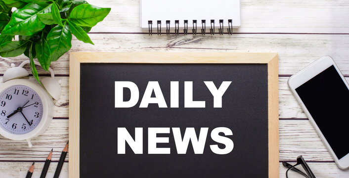 DAILY NEWS written on a black background near pencils, a smartphone, a white notepad and a green plant in a pot
