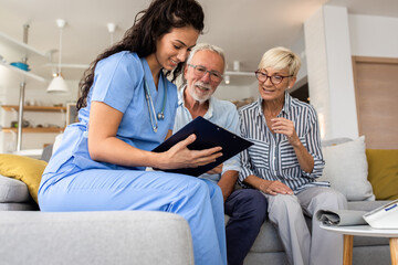 Female nurse talking to seniors patients while being in a home visit, senior couple signs an...