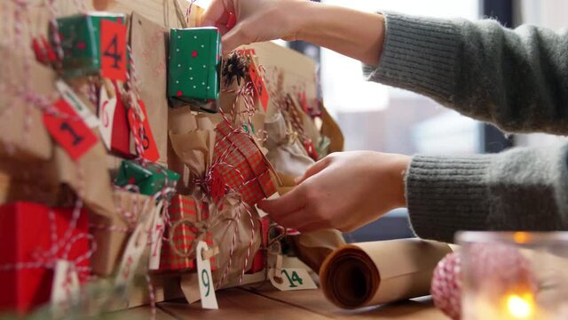 winter holidays, christmas and hobby concept - hands hanging gift box with tag to handmade advent calendar at home