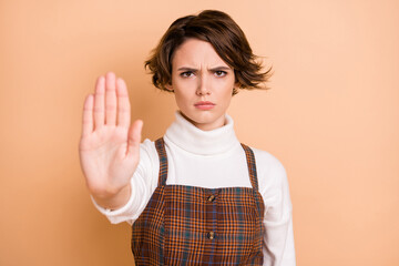 Photo of young serious unhappy frowning girl showing no stop sign in checkered overall isolated on pastel color background