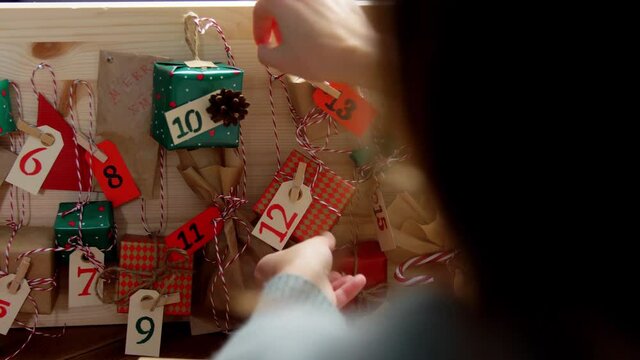 winter holidays, christmas and hobby concept - hands hanging gift box with tag to handmade advent calendar at home