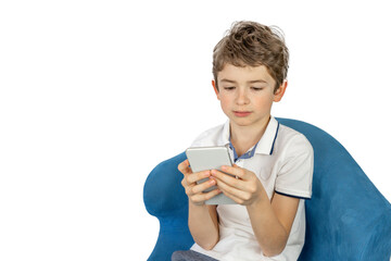 Fototapeta premium Young caucasian boy sitting in the armchair with smartphone and listening to music or playing game at home, isolated on white background. Technology and people or children concept