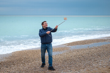 Young man blogger on the beach communicates with friends on a smartphone with a selfie stick