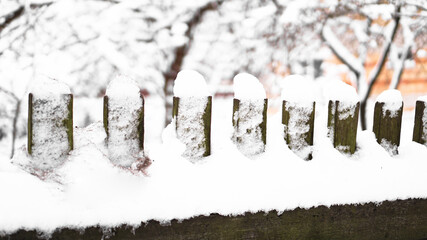 Wooden fence gate covered in white snow at heavy snowing snowstorm, bushes in background. Snow on a wooden fence as background image.