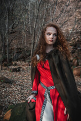 Red-haired woman in a red dress in a historical Celtic costume in the autumn forest