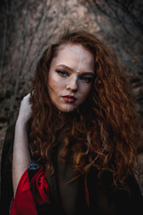 Red-haired woman in a red dress in a historical Celtic costume in the autumn forest