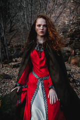 Red-haired woman in a red dress in a historical Celtic costume in the autumn forest