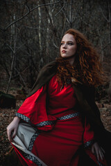 Fototapeta premium Red-haired woman in a red dress in a historical Celtic costume in the autumn forest