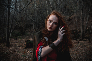 Red-haired woman in a red dress in a historical Celtic costume in the autumn forest