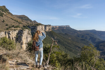Fototapeta premium Young woman with jeans and backpack looking into the distance horizon with hand in head .Amazing mountains landscape with forest.Traveling on holidays, vacation lifestyle concept.
