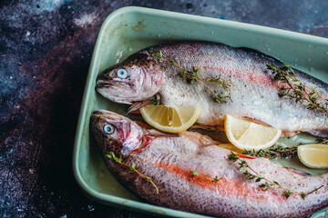 Fresh fish before cooking, seasoned with herbs, pepper, thyme and lemon. Fresh fish trout for baking on a dark kitchen background