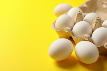 Egg box with fresh eggs on yellow background
