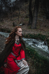 Red-haired woman in a red dress in a historical Celtic costume in the autumn forest