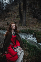 Red-haired woman in a red dress in a historical Celtic costume in the autumn forest