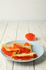 Plate of crepes with red caviar on white wooden background