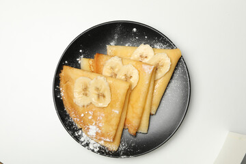 Plate of crepes with sugar powder and banana slices isolated on white background