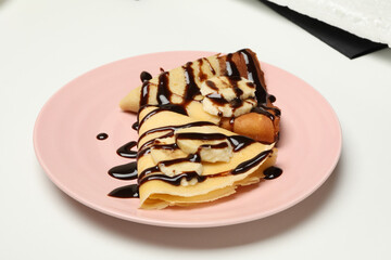 Plate of crepes with chocolate sauce and banana slices isolated on white background