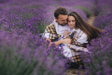 young couple are sitting and hugging at the lavender field together on summer day. love story. woman and man in plaid outdoors