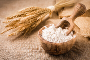 Flour in wooden bowl with grain on burlap background