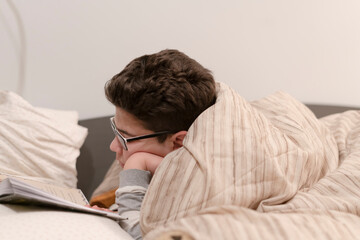 young man reading a book lying in bed before going to sleep to relax.