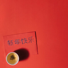 A Chinese tea cup with green tea on red surface. Red lucky envelope with 