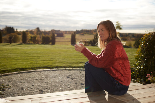 Young woman sitting on porch and drinking coffee