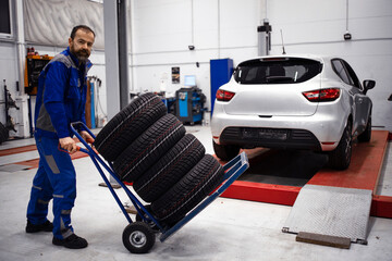Professional car mechanic with set of new tires standing in workshop by car. Changing tires for winter or summer season.