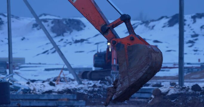 Earthwork at a construction site in winter, an excavator digs a place for a foundation, in the distance an excavator with a ripper tooth performs overburden works, softening the frozen soil