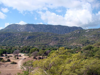 Obraz premium Amazing panorama of mountain ranges covered with green carpet of dense forests on a background of sunny blue and cloudy sky at the same time.