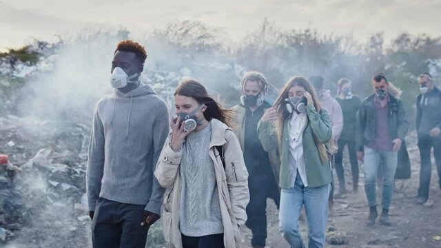 Group of Young Volunteers in Gas Masks Take Care of the Environment While Going Through the Toxic Smoke at Garbage Dump.Worldwide Global Problem of Pollution of Planet.Responsibility by the Future