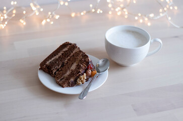 morning coffee in a white mug and a piece of chocolate cake with nuts, on a saucer, on a wooden table, with bokeh in the background. no focus. Hearty breakfast, sugar addiction. Allergenic foods, nuts