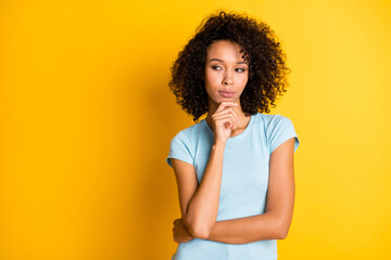 Photo of pretty serious dark skin wavy lady wear blue t-shirt arm chin looking empty space isolated yellow color background