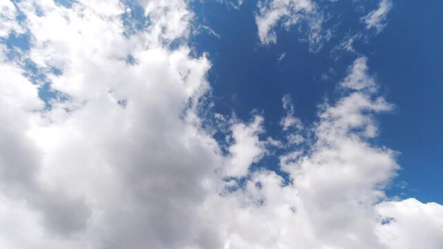 Time lapse clouds, rolling puffy cloud are moving, with blue sky in background.