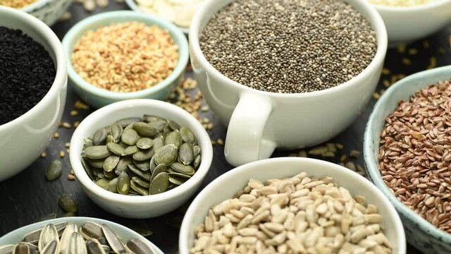 Assortment od healthy seeds - sesame, flax seed, sunflower seeds, pumpkin seed, chia and black seed in bowls on a black stone background. Top view