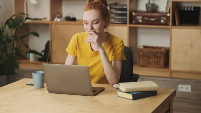A beautiful young redhead woman is working with her laptop sitting in the office