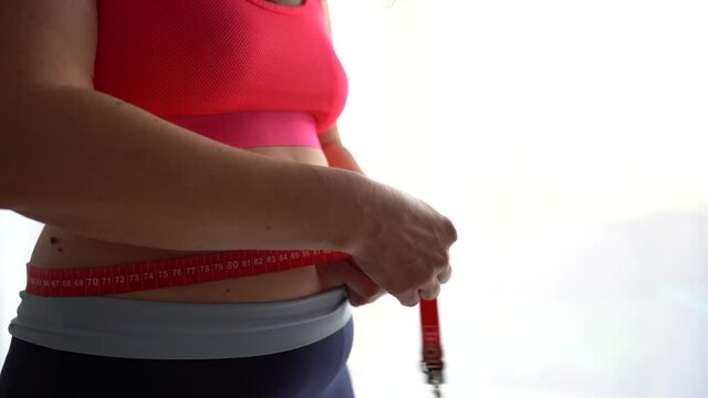 The girl measures the circumference of the waist with a measuring tape. Sports load, diet for weight loss, postpartum weight recovery
