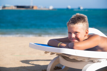 Blond Boy lying on Blue Sun Lounger on Beach and Sunbathe Summer Holidays