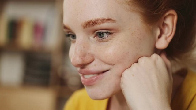 A close-up view of a smiling young redhead woman is watching her laptop sitting in the office