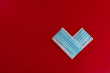 Two close-up blue medical masks stacked in the shape of a heart in red background with space for text. Theme of love banner. Loving, positive emotions. The concept of celebration and love..