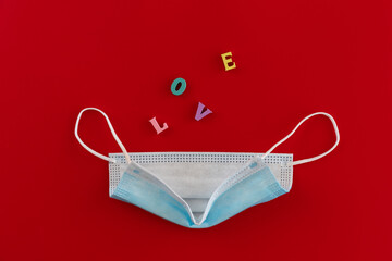Blue medical mask with wooden multicolored letters jumping with the inscription "LOVE" on red background. The concept of Valentine's Day and coronavirus. Theme of love banner. Loving, positive emotion