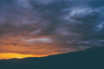 Atmospheric landscape with silhouettes of mountains with trees on background of vivid orange blue...