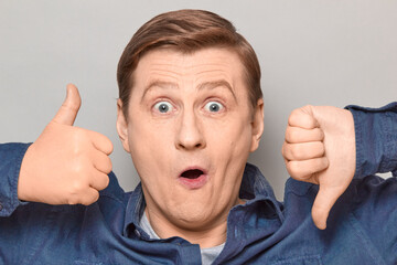 Portrait of surprised man showing thumb up and thumb down gestures