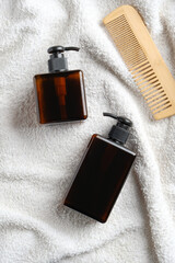 Hair care products on white towel in bathroom. Top view natural organic amber glass shampoo bottles and wooden hair comb.