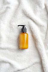 Yellow pump cosmetic bottle on white towel top in bathroom, top view. SPA natural beauty product packaging design.