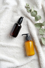 Natural herbal cosmetic. Amber glass bottle with serum, yellow dispenser bottle with body care lotions, eucalyptus leaf on white towel. Top view, flat lay.
