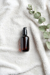 Natural herbal cosmetic. Amber glass bottle with serum and eucalyptus leaf on white towel in bathroom. SPA organic beauty product. Top view, flat lay.